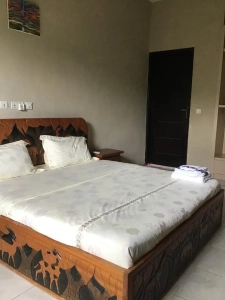 Chambre de la villa à louer à Bingerville avec lit en bois sculpté et linge blanc